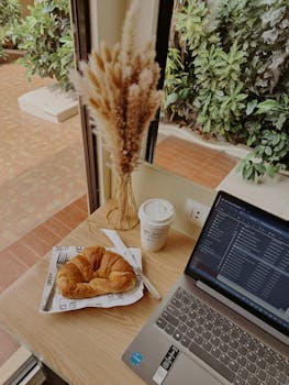 Warm workspace with a laptop, coffee, and croissant. Perfect for productivity or a relaxing break.