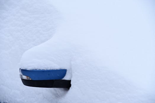 Close-up of a car mirror blanketed in snow, capturing a serene winter moment.