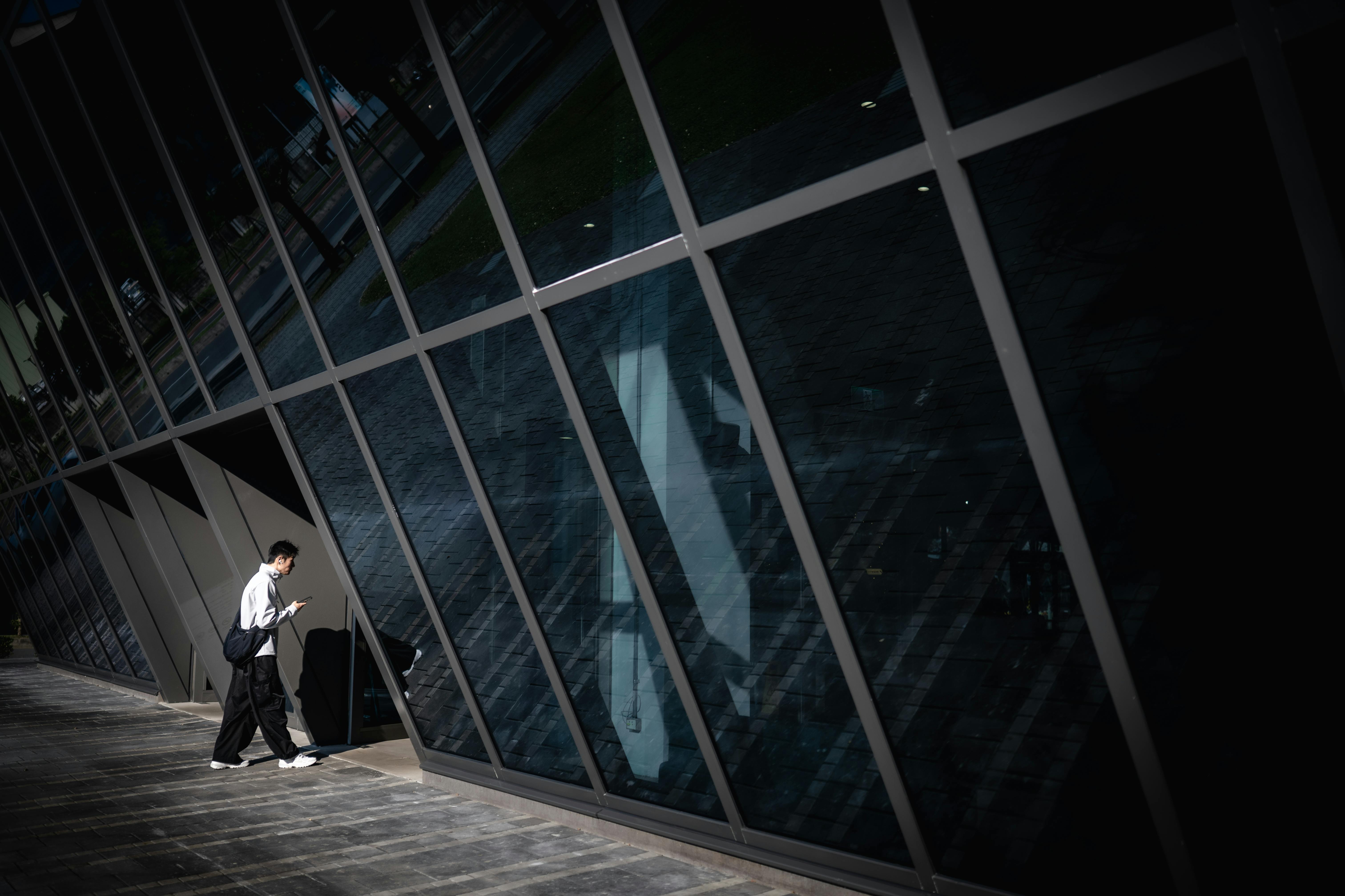 免費 一個人走過一座現代玻璃建築，映襯著都市建築。 圖庫相片