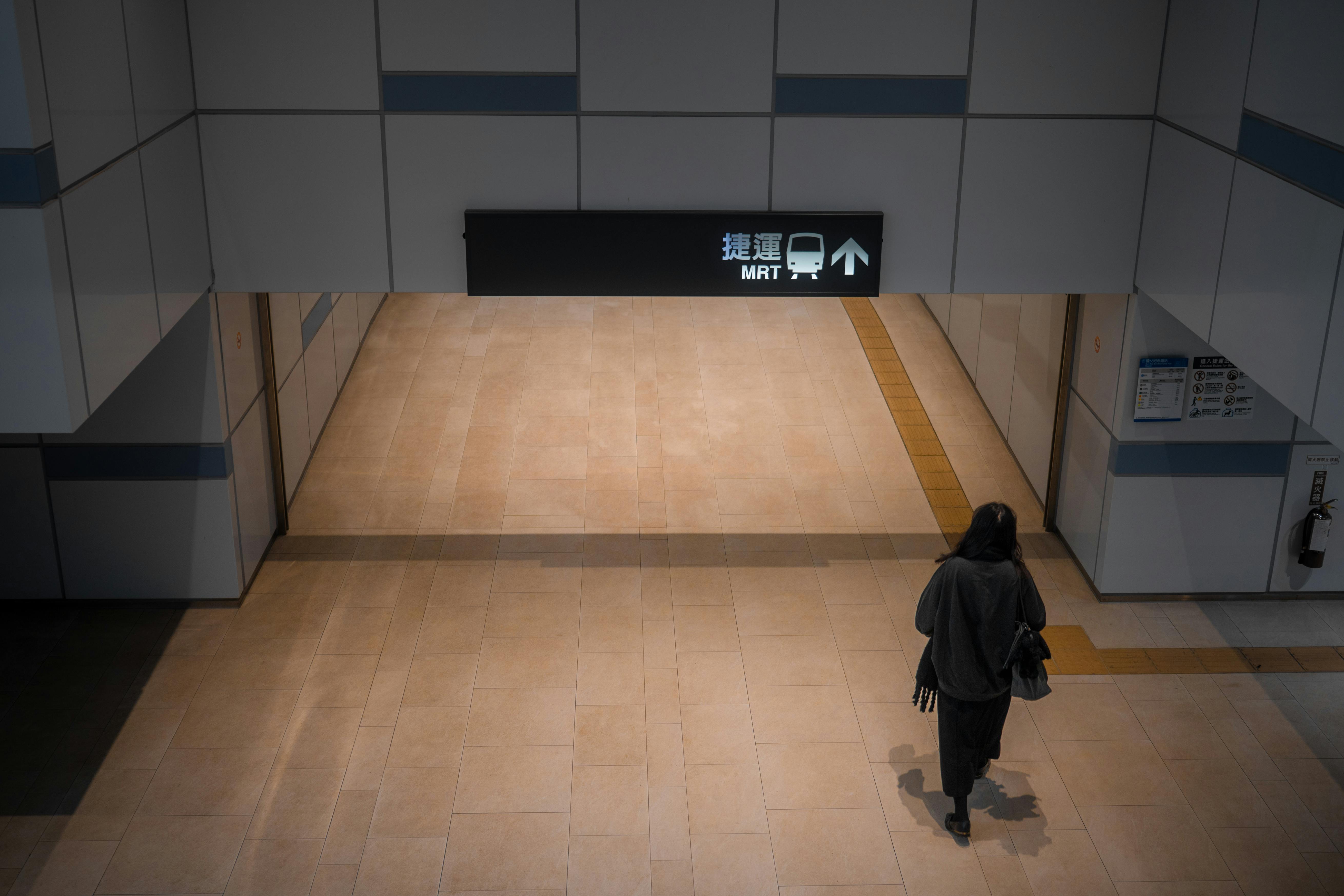 grátis Um passageiro solitário caminha em direção a uma entrada de metrô sinalizada com a sigla 'MRT' em uma estação coberta. Foto profissional