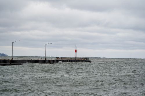 Free A lighthouse stands firmly on a pier amidst stormy waters under a cloudy sky. Stock Photo
