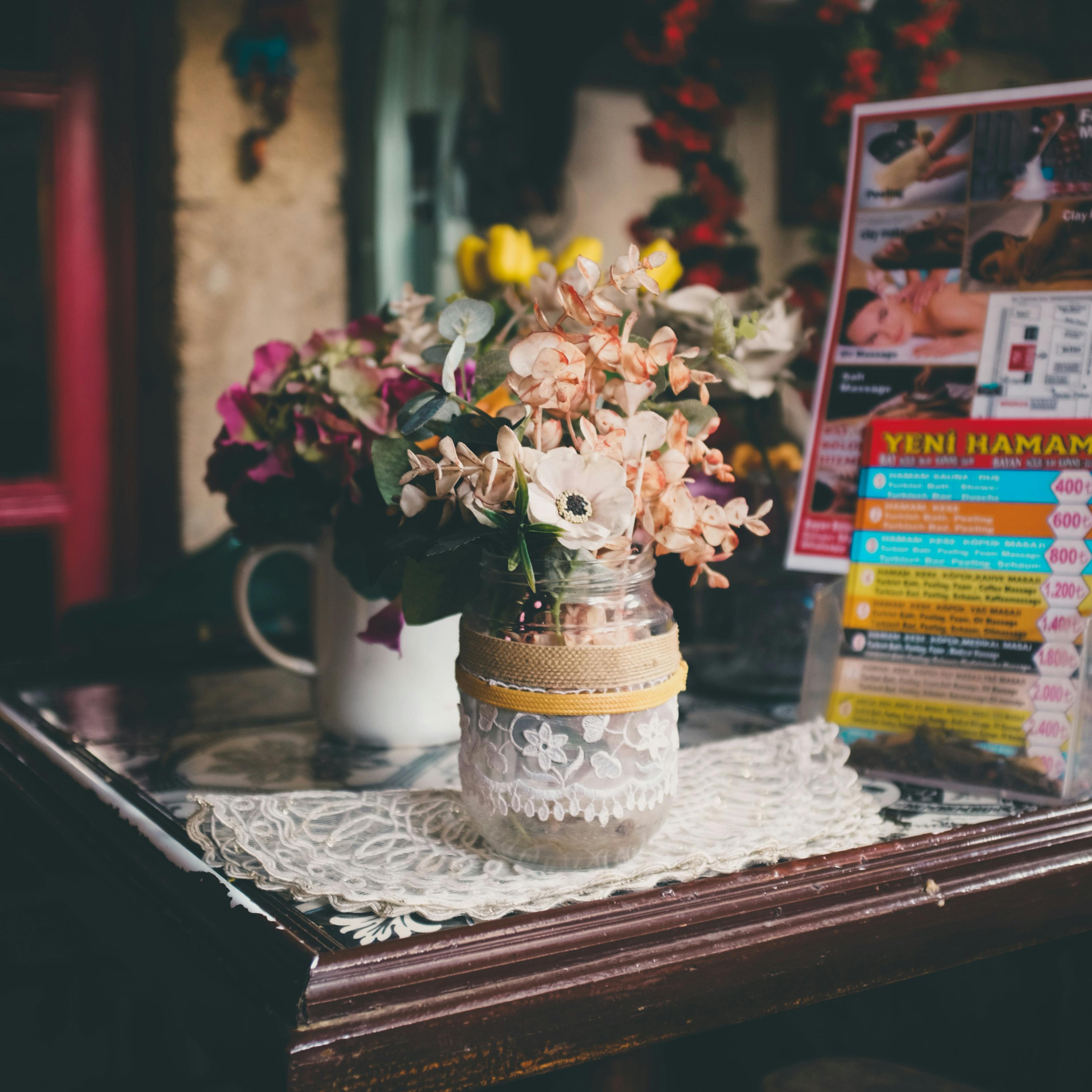 A charming floral bouquet in a decorated jar sits on a vintage lace doily, creating a cozy atmosphere.