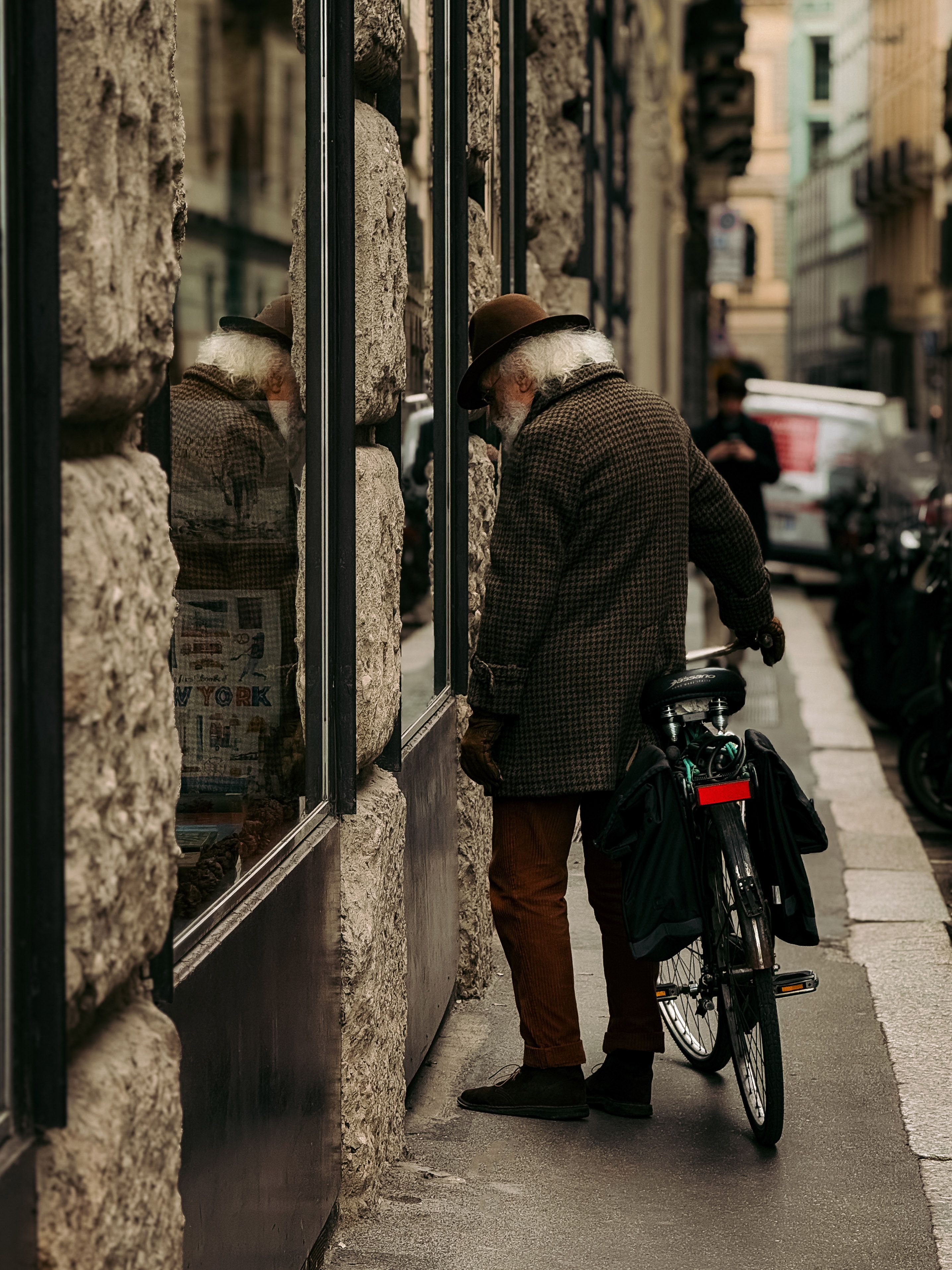 A stylish senior man with a bicycle stands thoughtfully by a shop window in Milan, Italy.