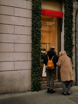 Adults gazing into Cartier shop during winter in Milan, Italy, with festive decorations.