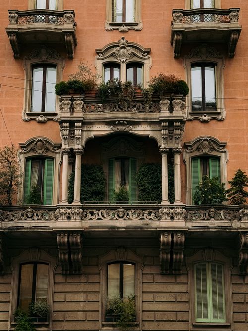 Free Detailed view of a classic Milanese building facade with ornate balconies and lush greenery. Stock Photo