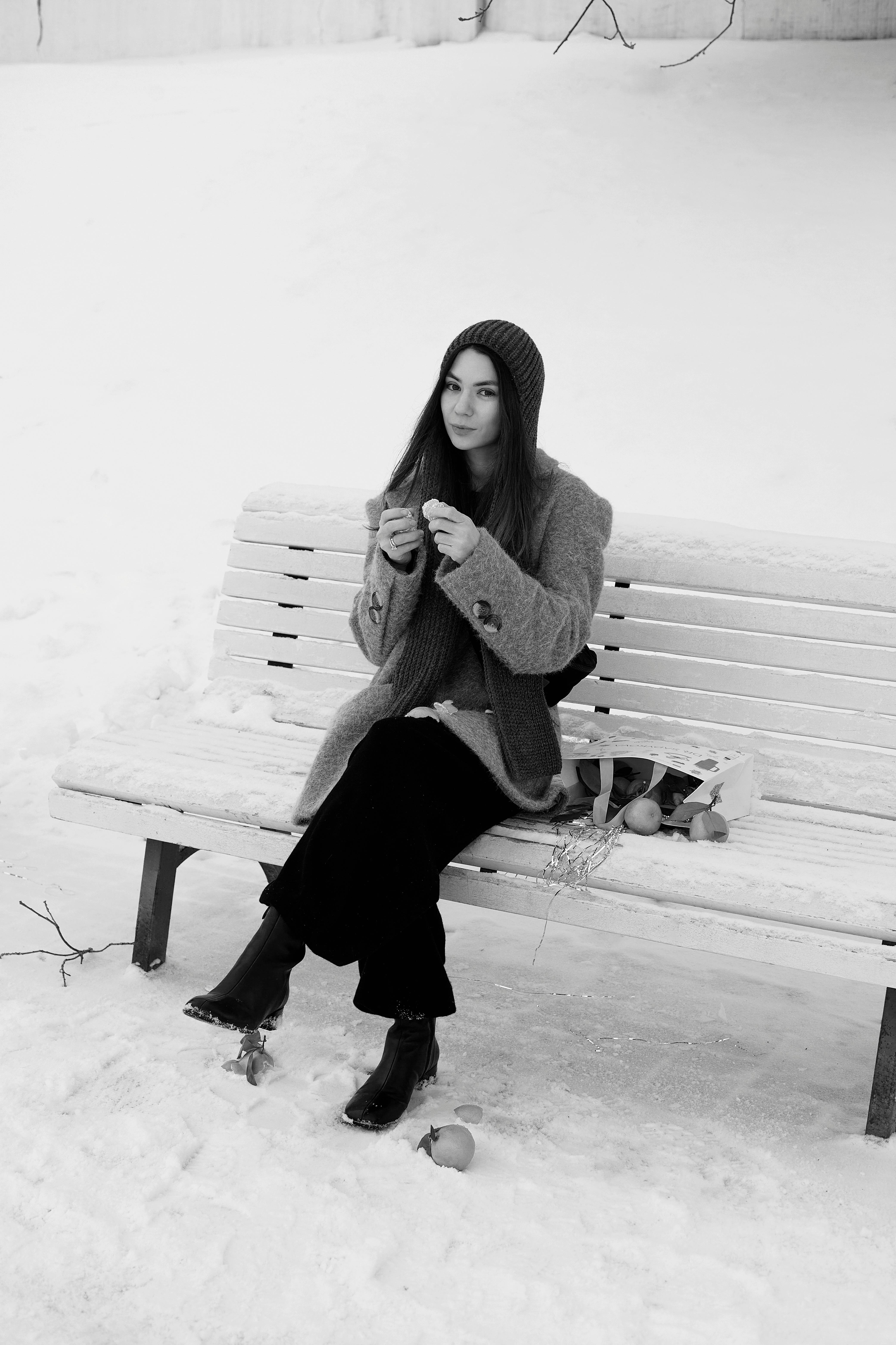 Kostenlos Eine Frau sitzt in Winterkleidung auf einer Bank in einem verschneiten Park und strickt. Stock-Foto