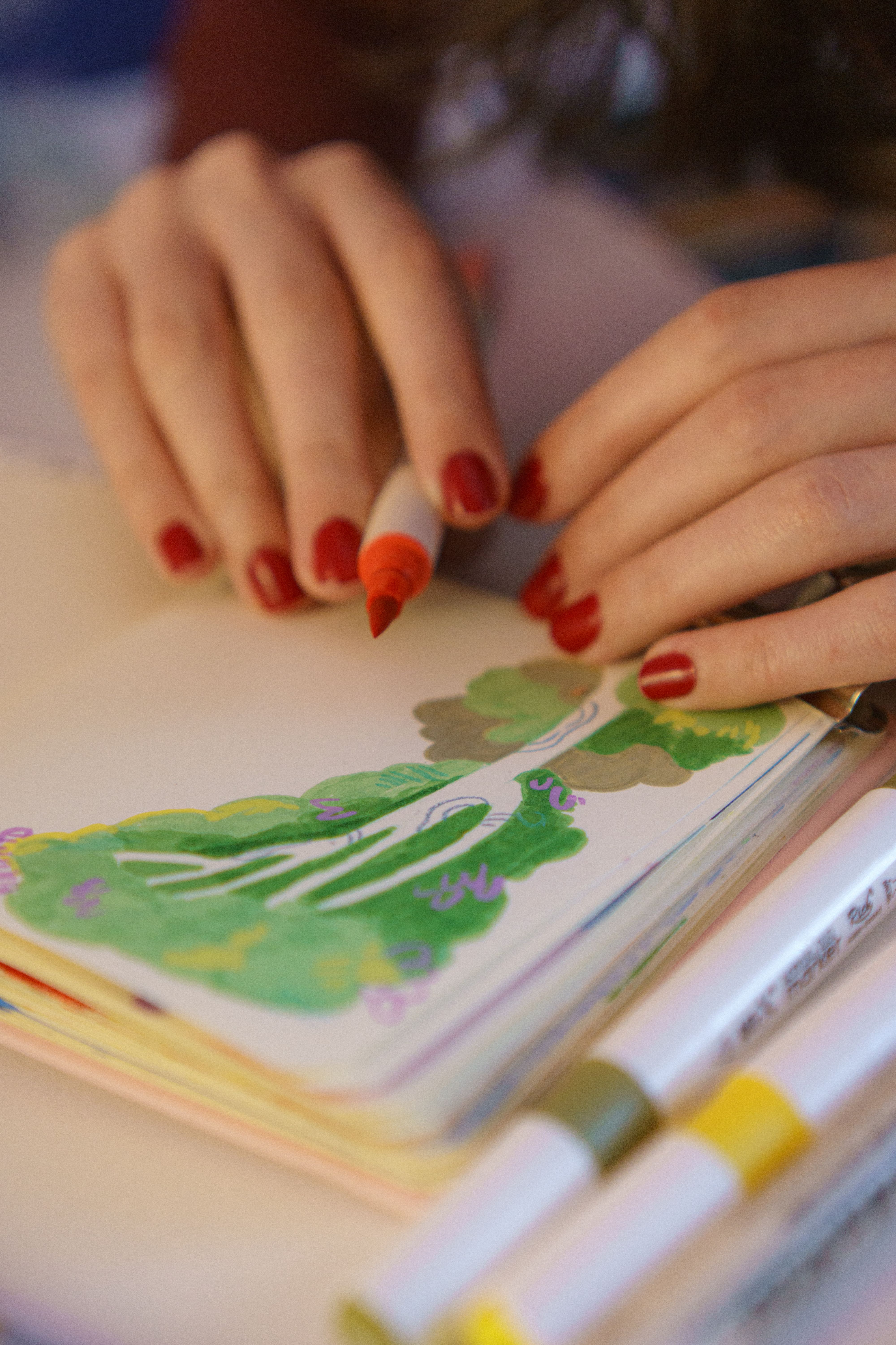 Hands drawing a colorful tree with markers in a sketchbook.