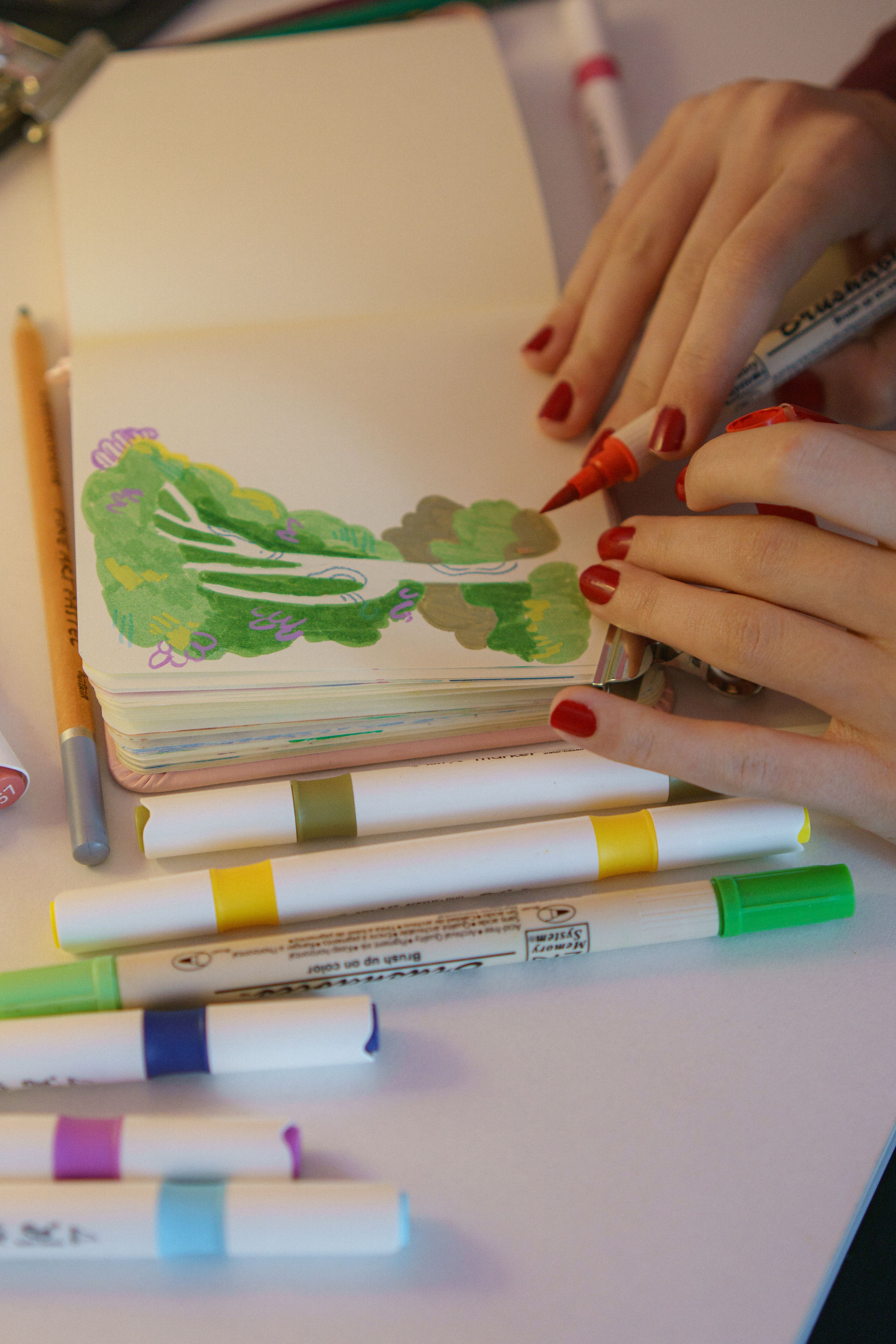 Hands drawing in a sketchbook using vibrant markers, showcasing creativity and artistic expression.