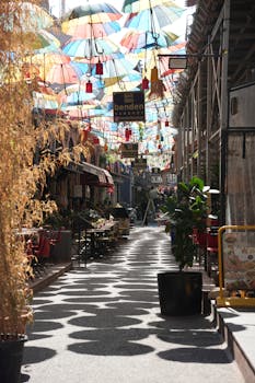 A narrow street adorned with colorful umbrellas casting playful shadows on a sunny day.