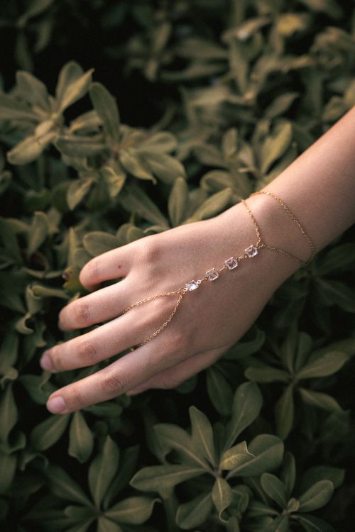 Free A delicate gold hand bracelet elegantly displayed over lush green leaves, perfect for fashion and lifestyle. Stock Photo