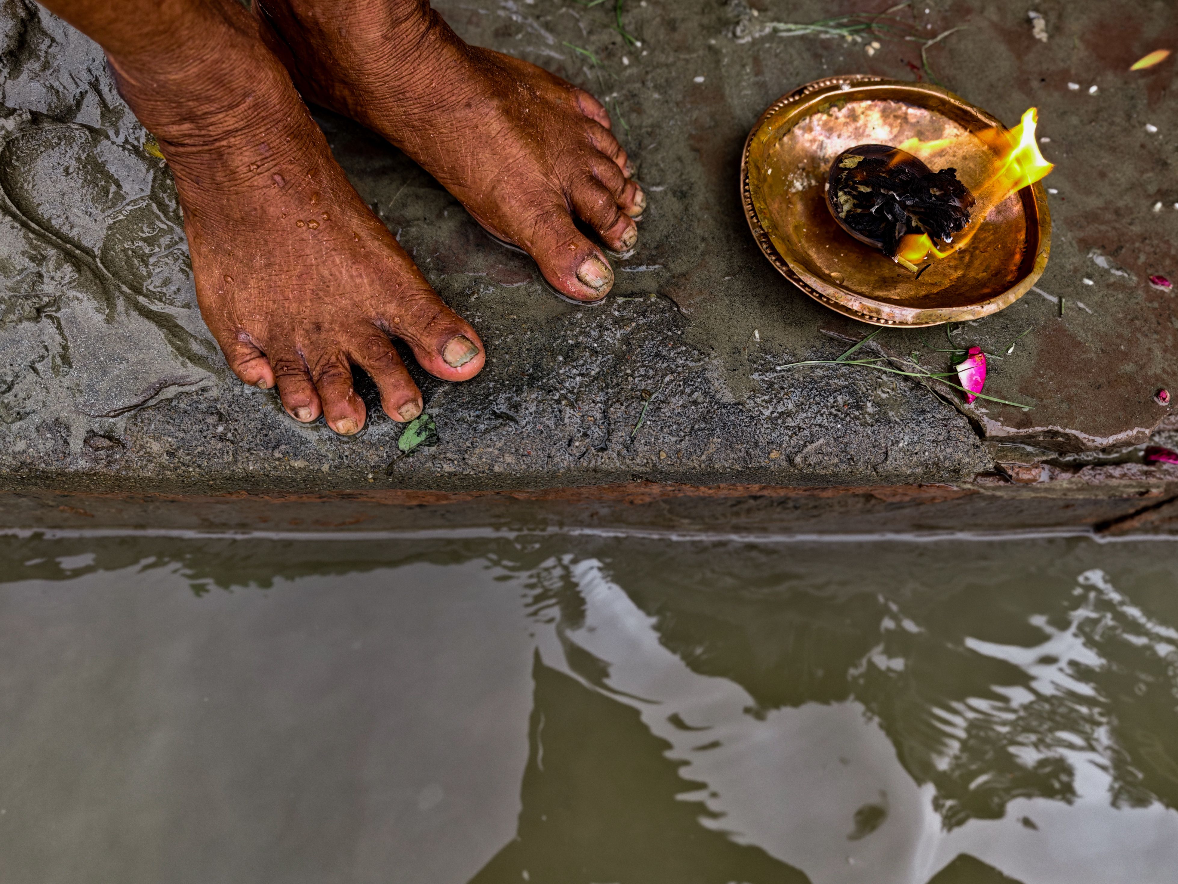 Barefoot ritual beside the water featuring a lit offering on a brass plate.