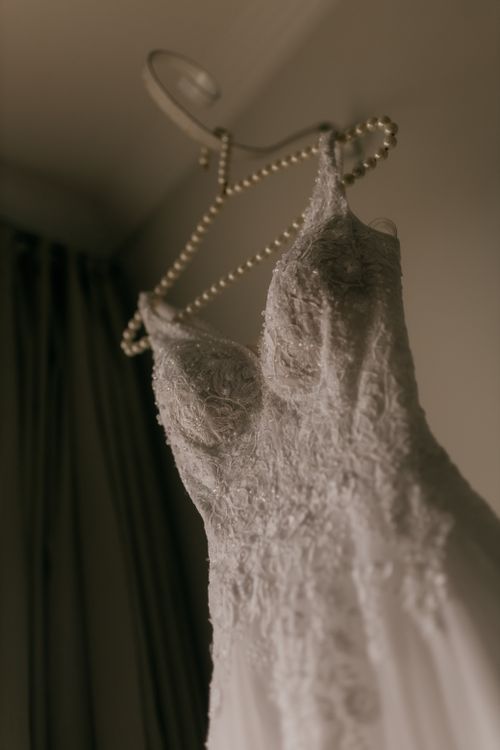 Free Sophisticated white lace wedding gown elegantly hung on a pearl hanger in soft lighting. Stock Photo