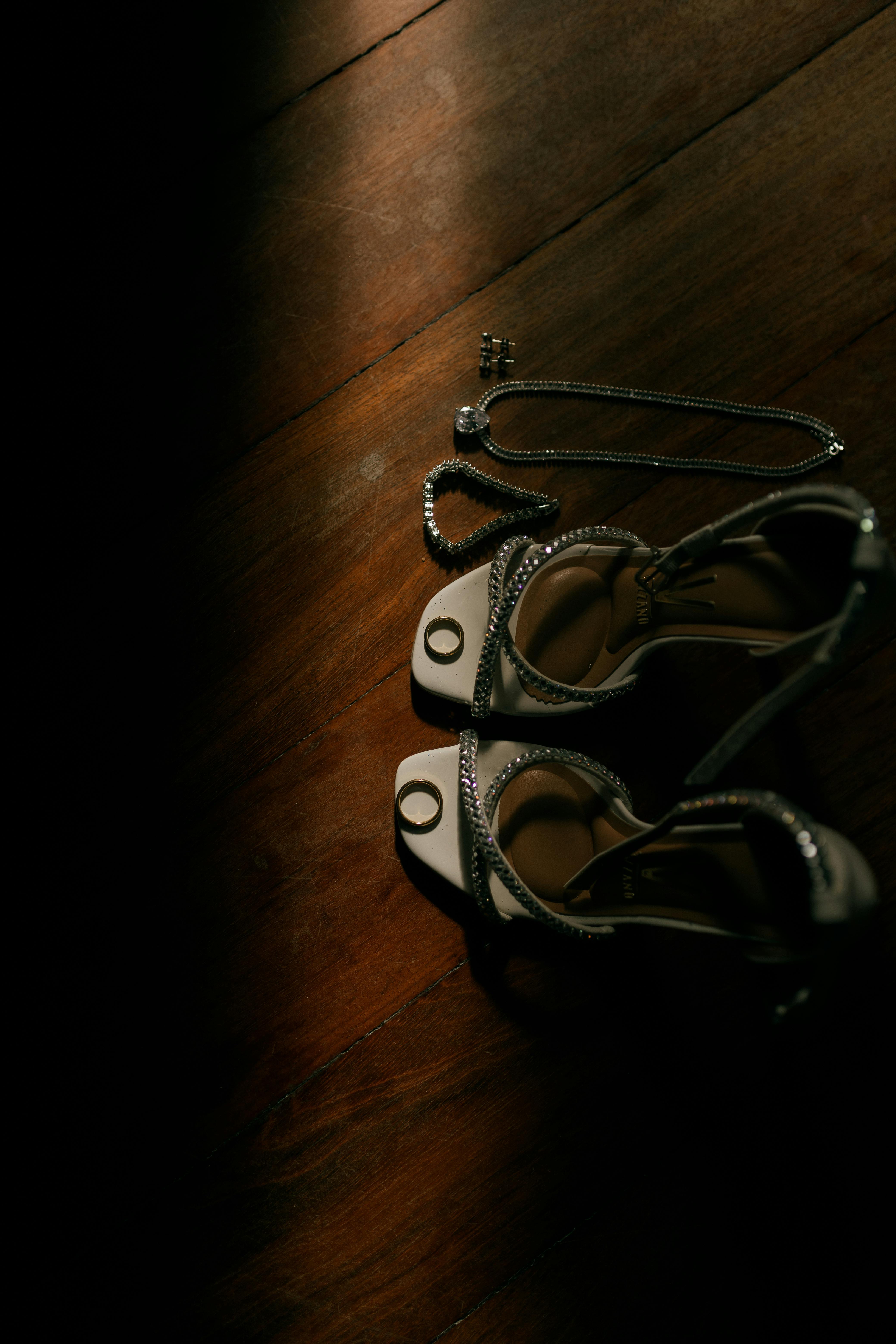 Gratis Primer plano de zapatos de novia y joyas con una iluminación suave sobre un suelo de madera. Foto de stock