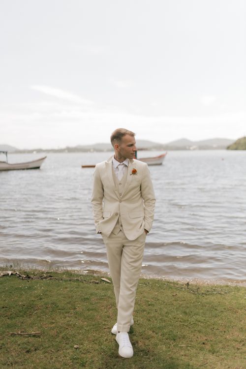 Free A groom in a beige suit stands by the lake, embodying a serene and elegant scene. Stock Photo