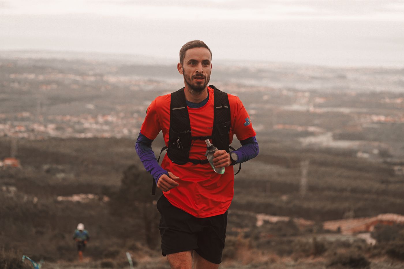 A man trail running on a scenic mountain path with an open, elevated landscape view.