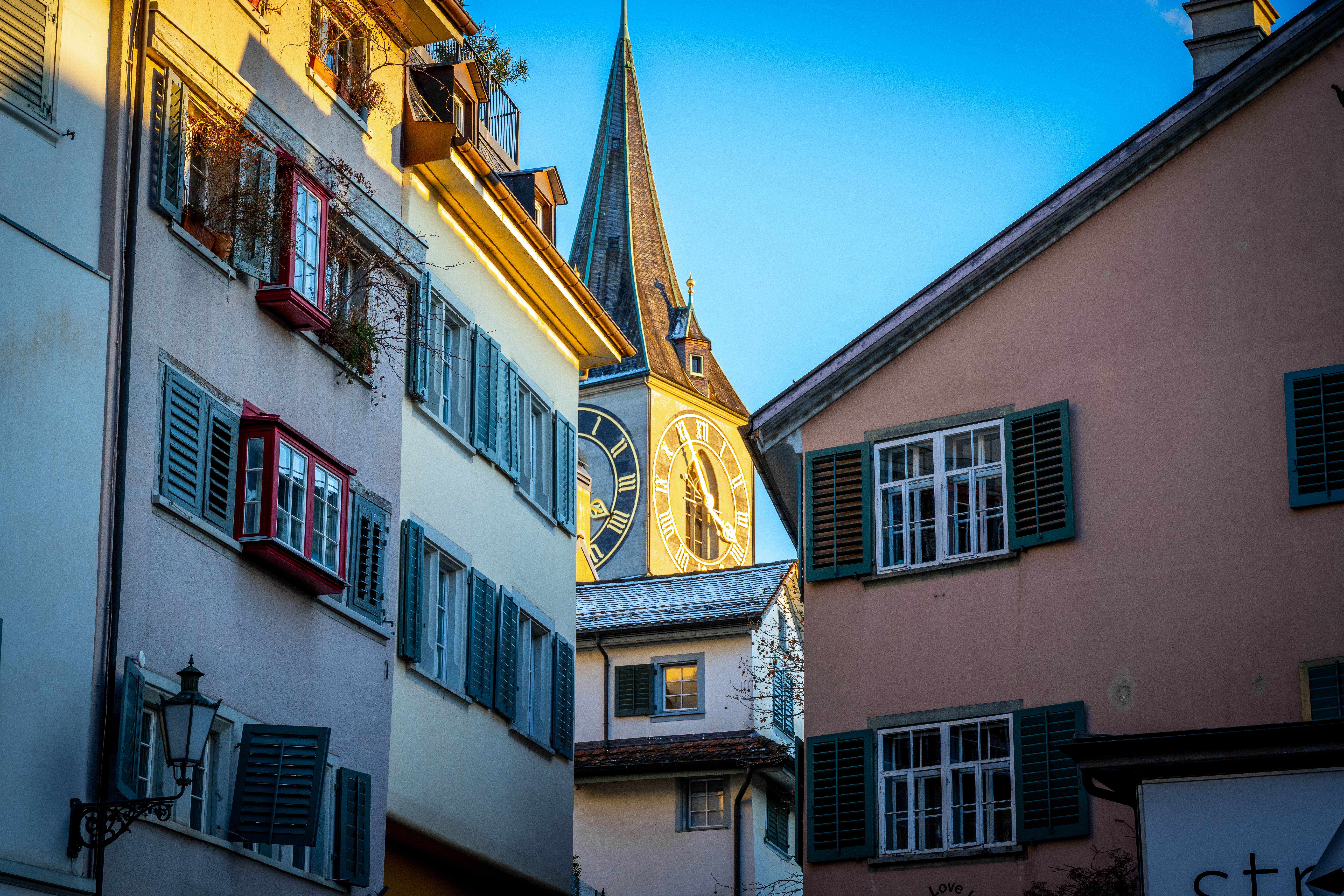 Charming view of St. Peter's Church clock tower framed by traditional Swiss architecture in Zurich.