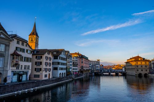 Free Beautiful view of Zurich cityscape along the Limmat River featuring St. Peter's Church at sunset. Stock Photo