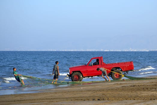 Pescatori al lavoro su una spiaggia dell'Oman, tirando le reti con un pick-up rosso in riva all'oceano.