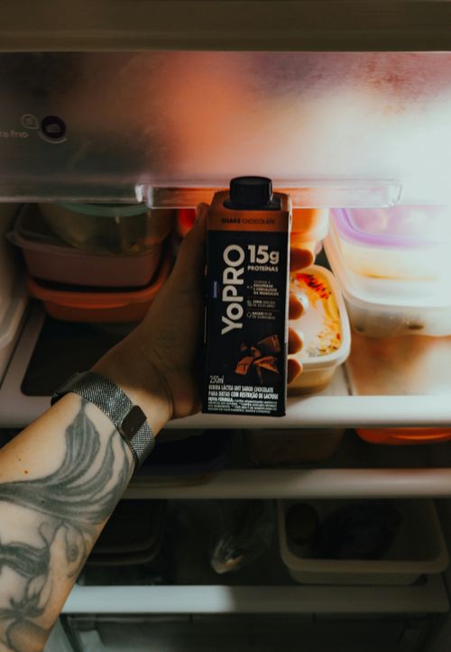 Free Tattooed arm holding a chocolate protein drink in an open refrigerator. Stock Photo