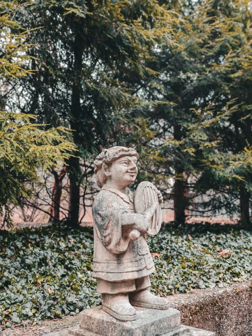 Free Stone statue depicting a playful figure with a musical instrument in a lush garden. Stock Photo