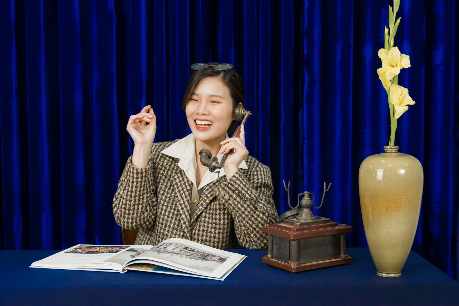 Woman in retro attire smiling while using a vintage phone, with a decorative vase on a table.