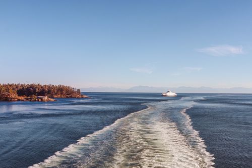 Free A ferry moves across calm sea near a wooded island under a clear blue sky. Stock Photo