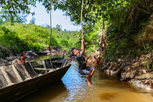 Joyful kids swinging over a tranquil jungle river in North Sumatra, Indonesia.
