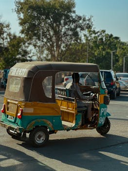 A vibrant tuk-tuk with a driver on a sunny street, showcasing urban mobility.