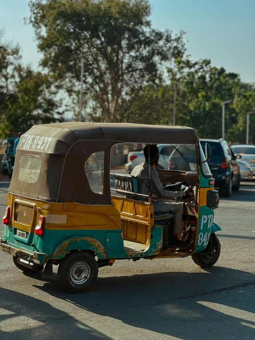 Free A vibrant tuk-tuk with a driver on a sunny street, showcasing urban mobility. Stock Photo
