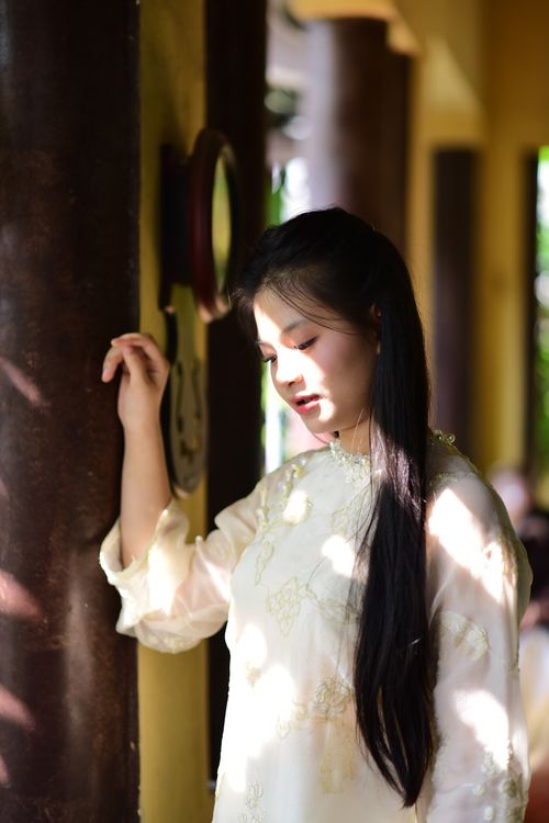 Free A woman in traditional attire stands pensively by a sunlit column indoors. Stock Photo
