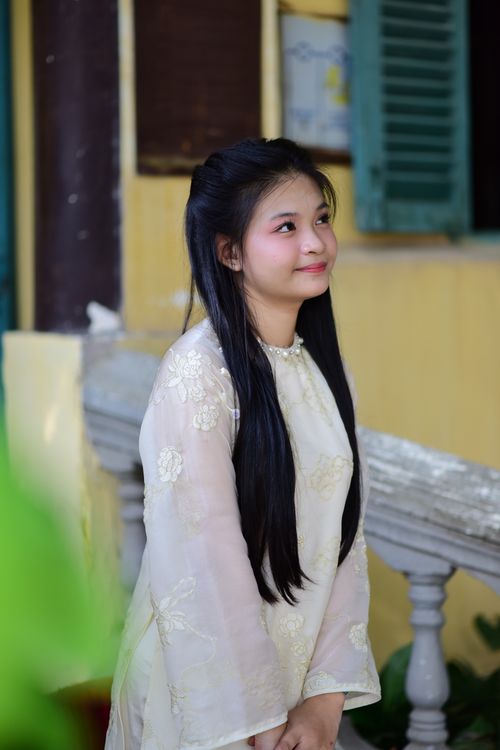 Free A young woman in a traditional Vietnamese dress stands outside, looking serene and peaceful. Stock Photo