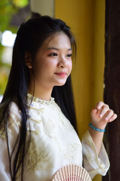 Free Young Asian woman in elegant traditional dress, standing near window with natural light. Stock Photo