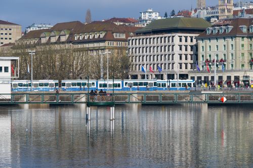 Free Tram crossing a bridge in Zurich with historic buildings in the background on a clear day. Stock Photo