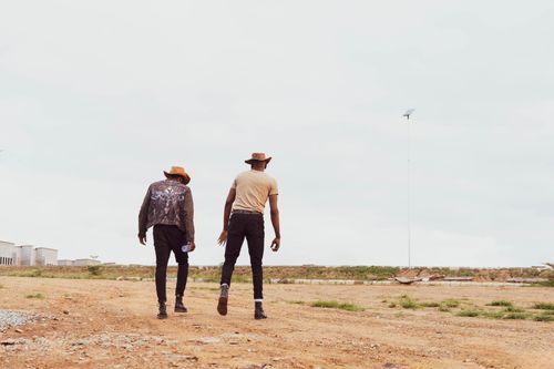 Free Two men in cowboy attire walking on a dirt path, showcasing western fashion. Stock Photo