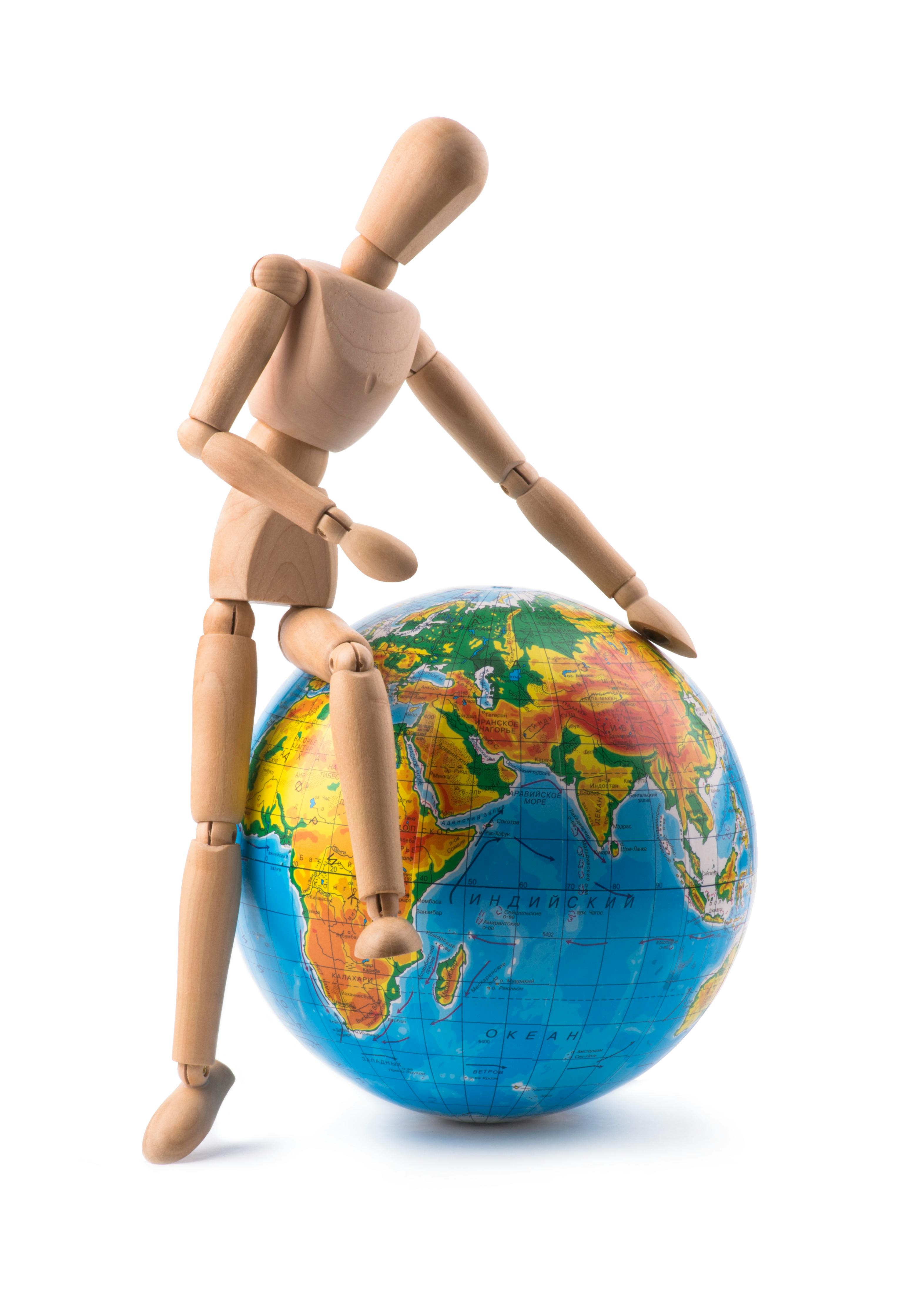 Zadarmo Drevená figurína kreatívne sedí na farebnom glóbuse a symbolizuje globálnu jednotu. Fotka z fotobanky