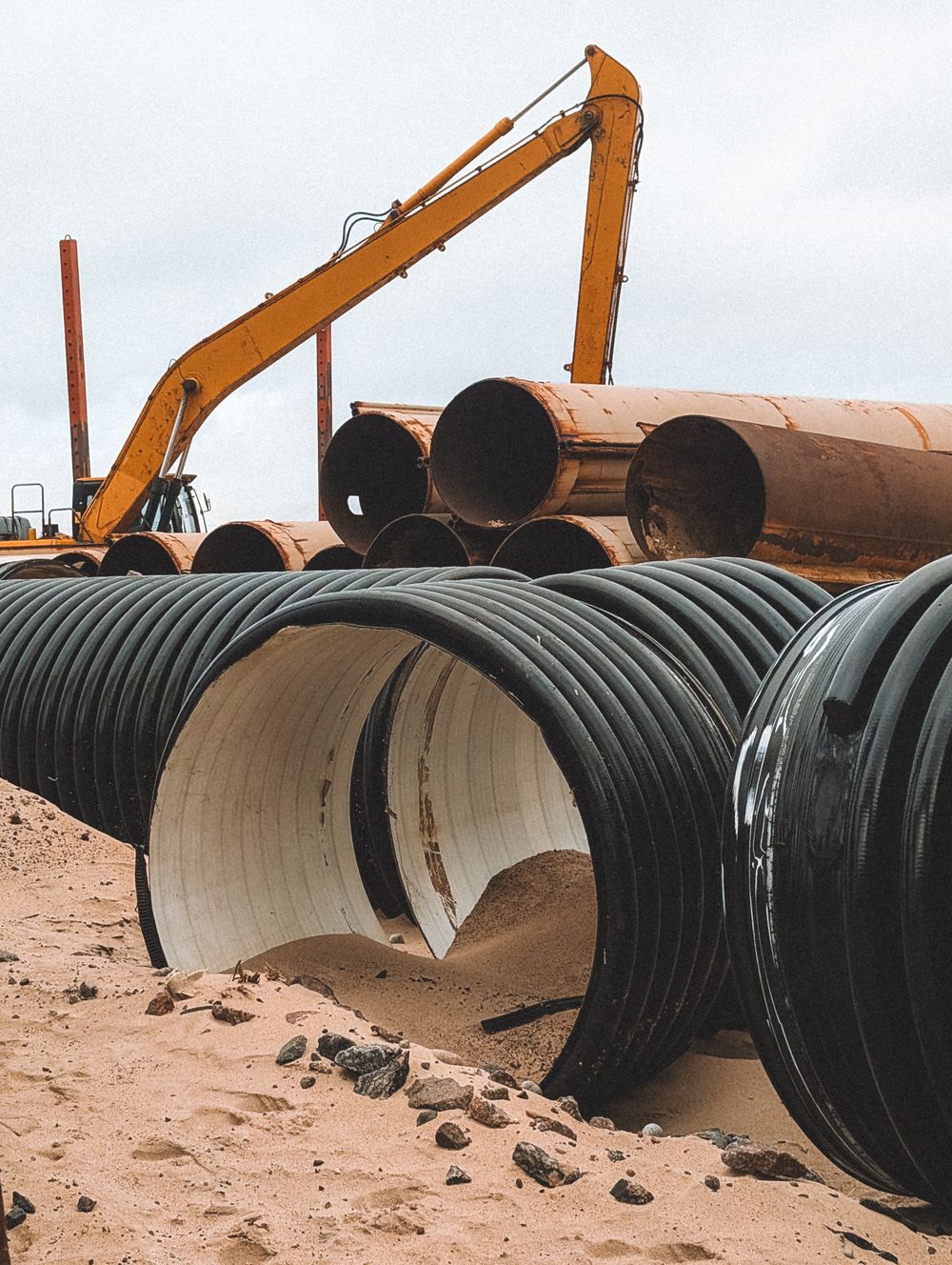 Coils of new continuous HDPE pipe staged beside heavy equipment for a replacement pull