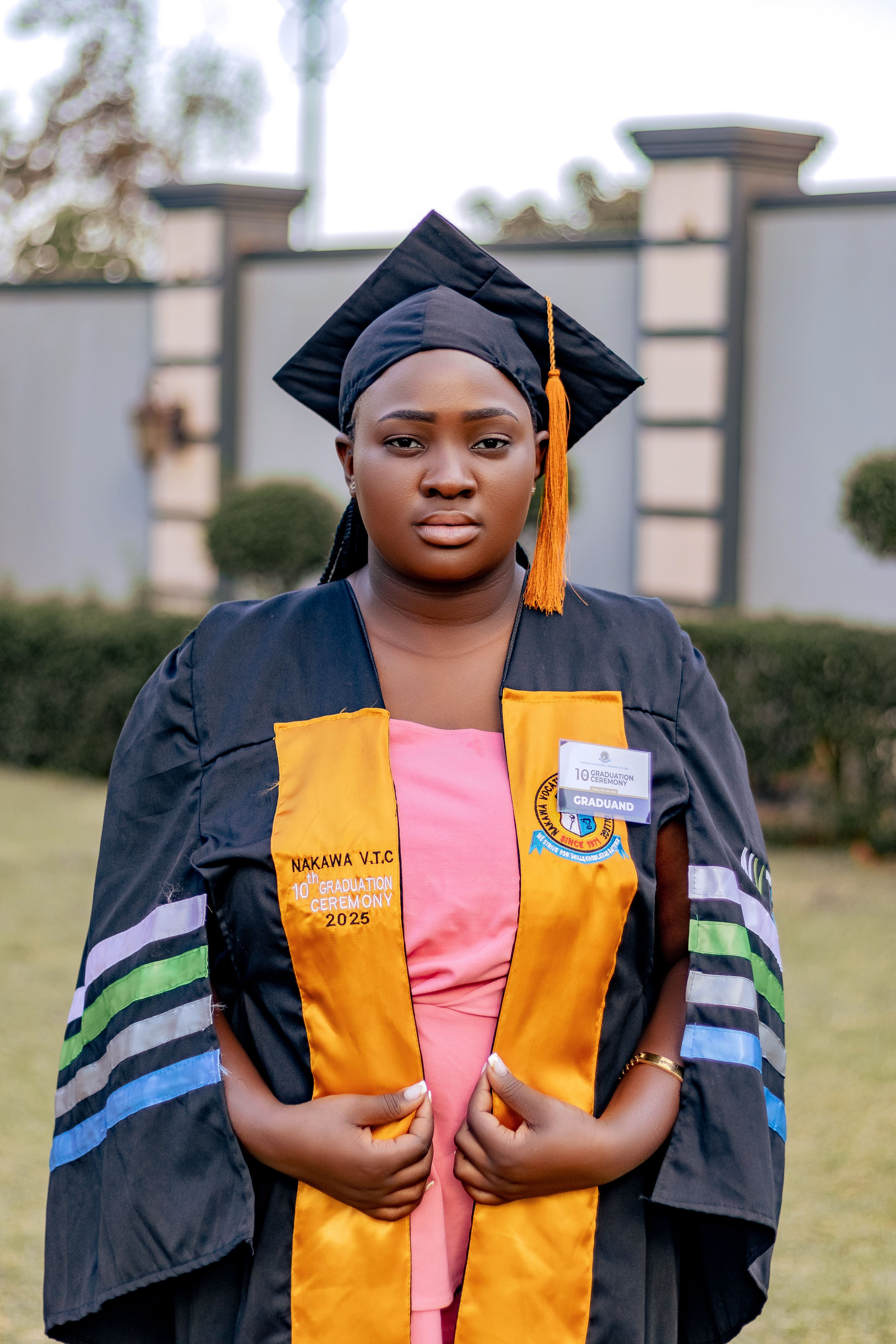 Graduating student poses proudly in academic regalia outdoors, signifying achievement.