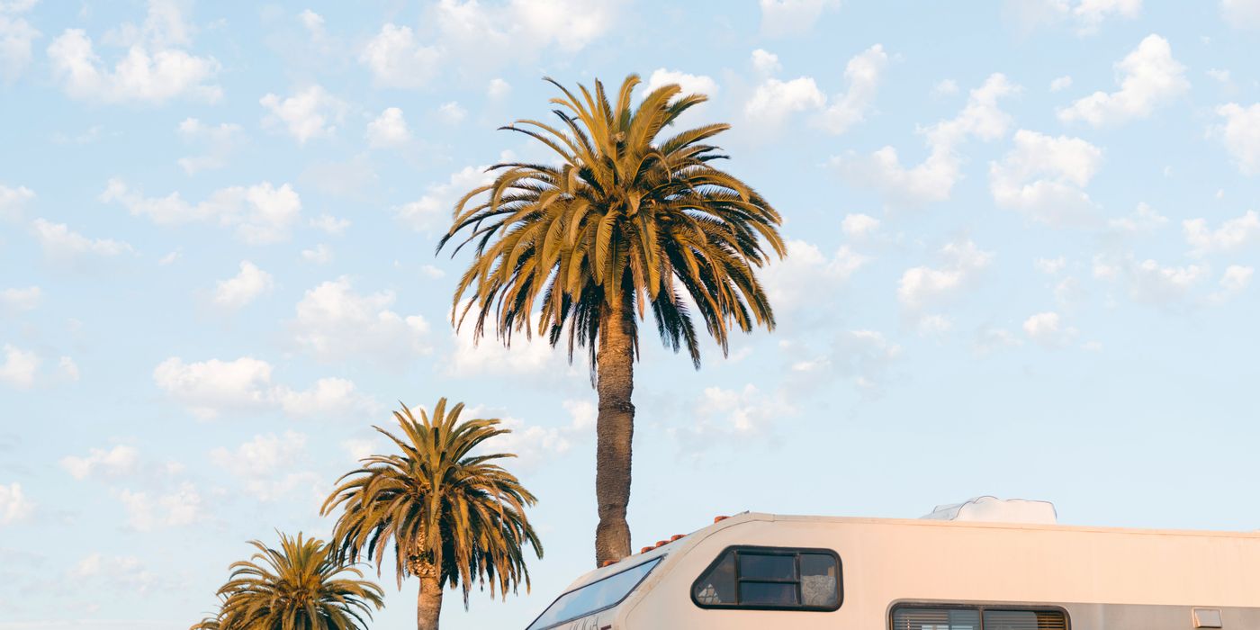 An older Class C motorhome parked in a lot under palm trees
