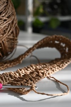 Detailed view of brown crochet yarn and hook in bright light, perfect for craft enthusiasts.