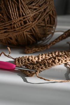 Detailed view of a crochet hook with yarn in progress on a sunny table.