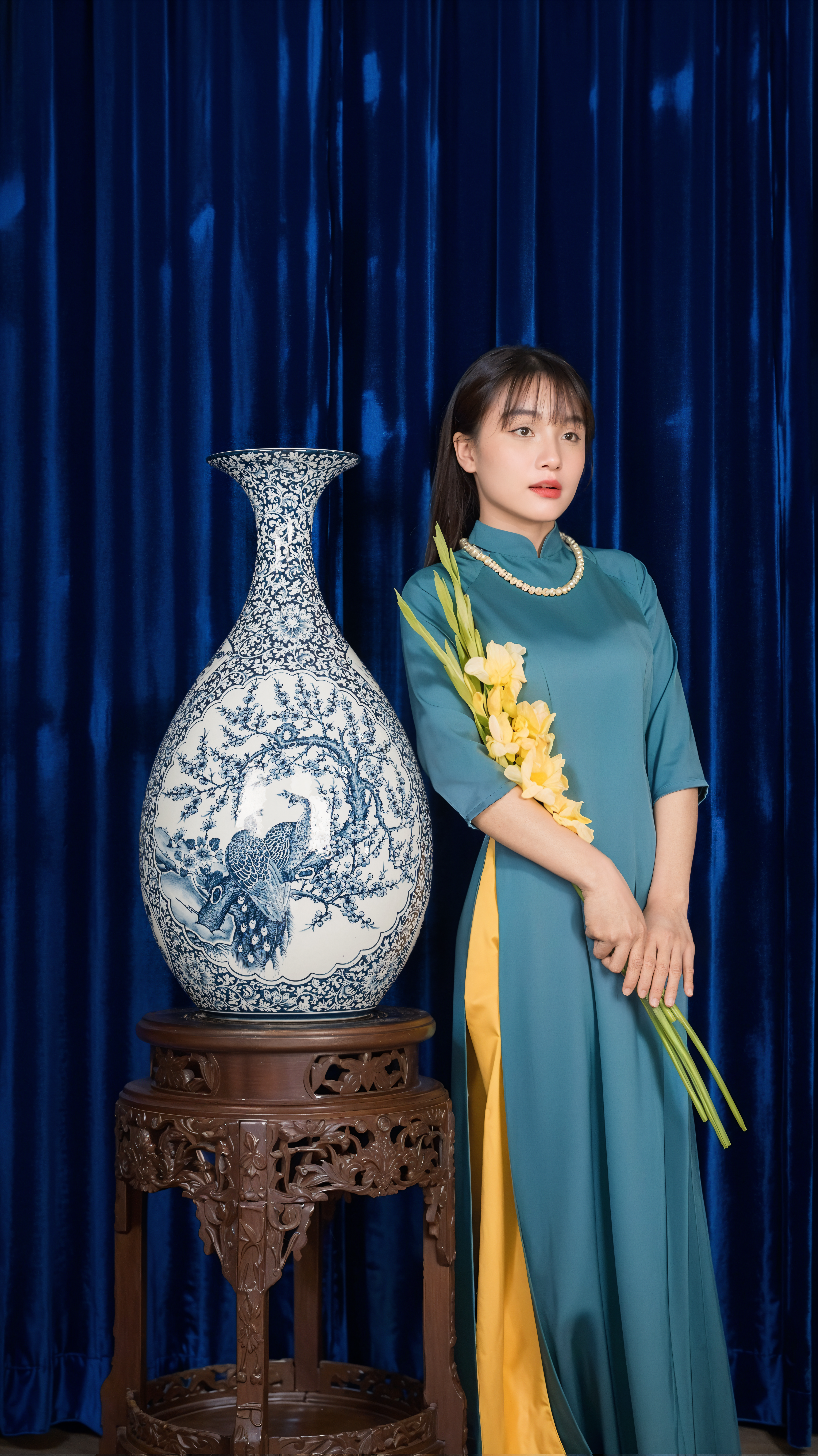 Woman in traditional Ao Dai beside a large ornate blue and white vase indoors.
