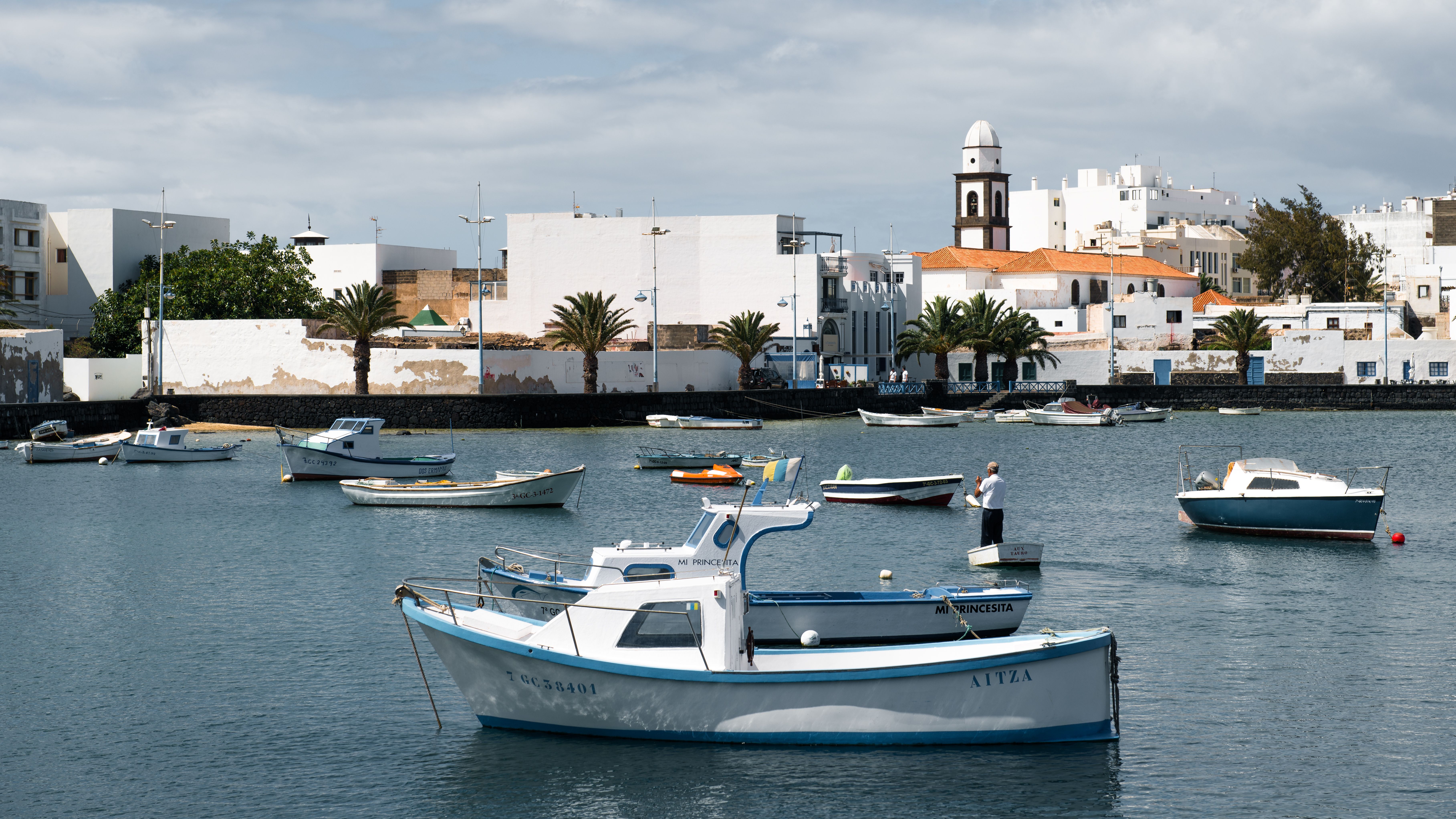Scenic view of fishing boats in a tranquil Lanzarote harbor with historic architecture.