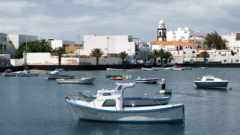 Scenic view of fishing boats in a tranquil Lanzarote harbor with historic architecture.