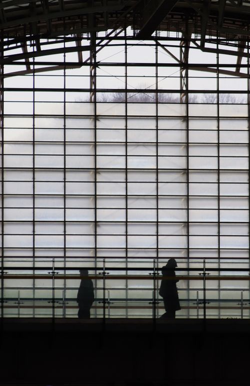 Free Two people silhouetted against large glass panels in a modern indoor setting. Stock Photo