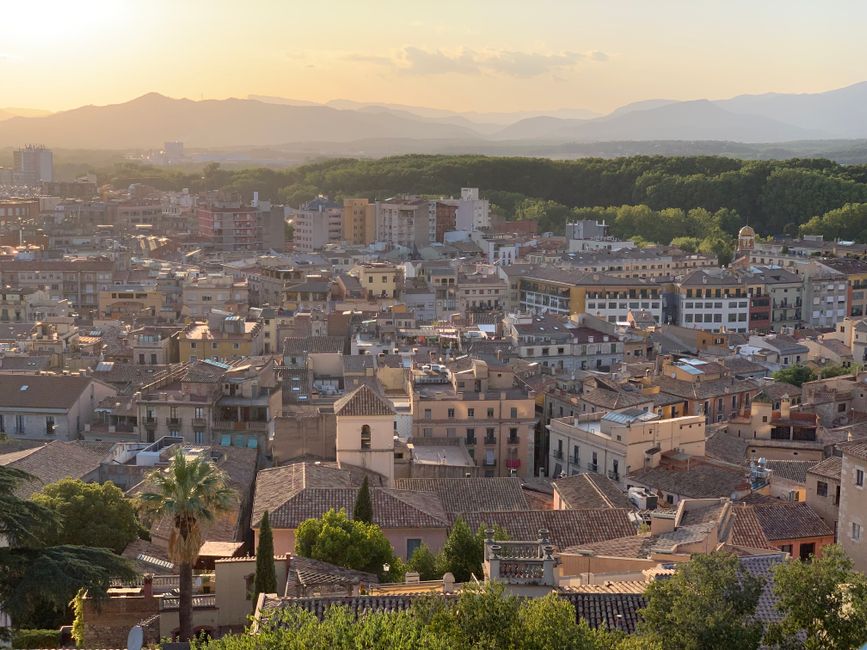 Una vista impresionante del paisaje urbano de Girona al atardecer, con montañas distantes y exuberante vegetación.