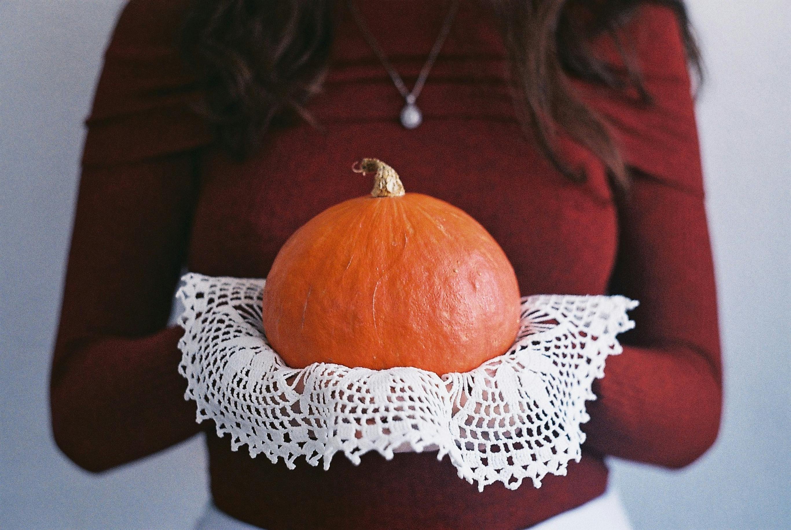 A woman holds a pumpkin with a lace cloth, set against a fall theme.