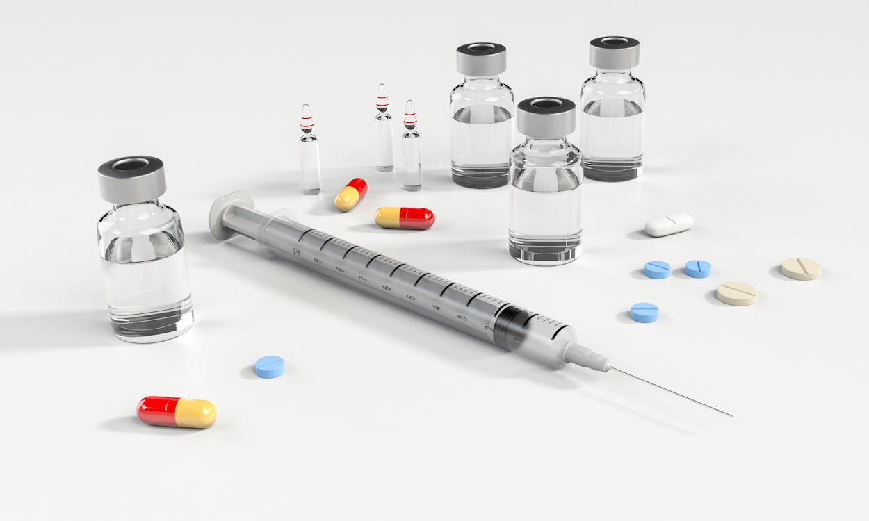 Syringe and Glass Bottle Beside Pills
