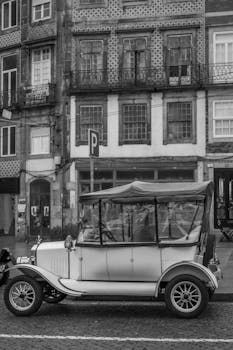 Black and white photo of a vintage car in front of historic buildings in Porto, Portugal.