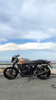 Vintage motorcycle parked on an oceanfront road with a scenic sky backdrop.