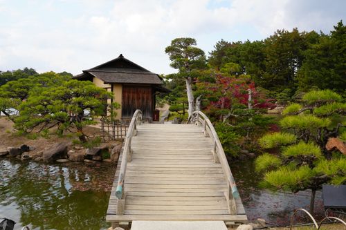Free A peaceful view of a wooden bridge in Okayama Korakuen Garden, Japan, highlighting traditional Japanese architecture and lush greenery. Stock Photo